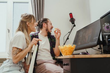 Video oyunu oynarken peynirli börek yiyen ya da evde internetten bir şeyler izleyen genç çift.