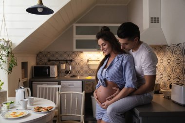 Bebek bekleyen genç ve şehvetli bir çift. Koca ve hamile karısı kahvaltı saatinde rahat mutfakta..