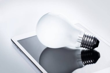 Beyaz tablet bilgisayarda duran ampulün kapanışı. İş dünyasındaki yenilik ve çözümler kavramı.