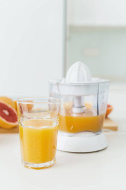 Bir bardak portakal suyu, narenciye suyu ve beyaz mutfak masasında çeşitli narenciye meyveleri.