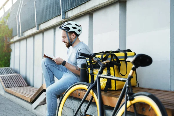 Genç Ekspres Kurye Bankta Oturuyor Yalıtımlı Çanta Bisikletli Bir Kitap — Stok fotoğraf