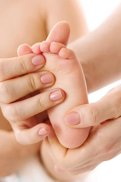 Closeup shot of a mother gently massaging her little child\'s feet and soles on white background.