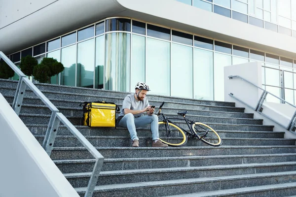 Genç Ekspres Yemek Kuryesi Izole Edilmiş Çanta Bisikletle Merdivenlerde Oturuyor — Stok fotoğraf