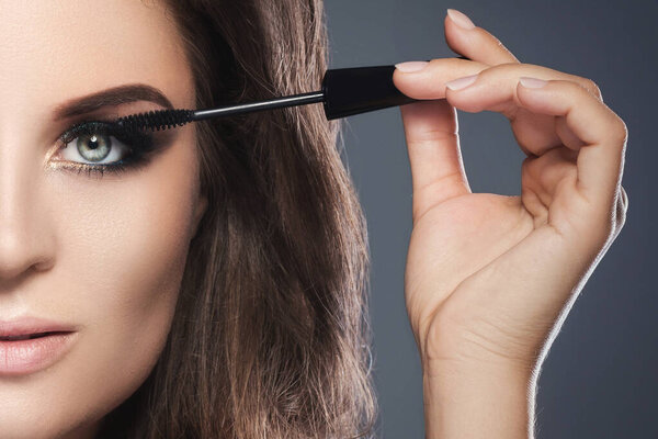 Stunning woman with beautiful make-up is applying mascara on her lashes