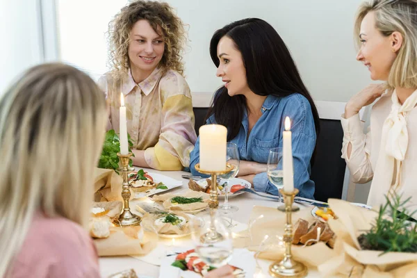 年轻快乐的女性朋友们在节庆桌上聊天 桌上摆满了食物和白葡萄酒 点缀着蜡烛 — 图库照片