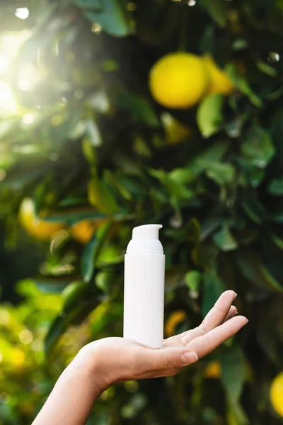 Frau Hält Weiße Flasche Hautpflegemittel Der Hand Auf Verschwommenem Zitronenbaum — Stockfoto