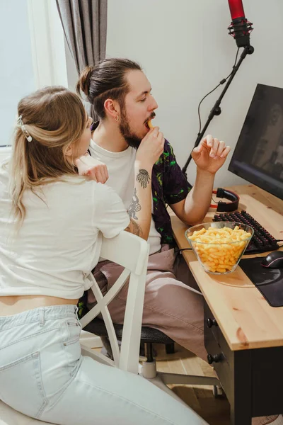 Νεαρό Ζευγάρι Τρώει Cheese Puffs Παίζοντας Βιντεοπαιχνίδια Βλέποντας Κάτι Online — Φωτογραφία Αρχείου