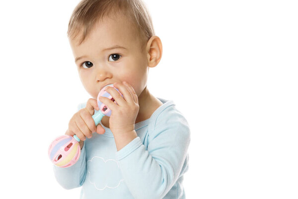 Adorable little boy in a romper is playing with plastic rattle and putting it in his mouth on white background.