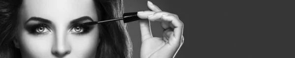 Stunning woman with beautiful make-up is applying mascara on her lashes