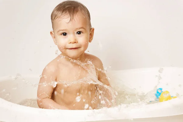 可爱的小男孩微笑着 一边用漂浮的橡胶玩具洗澡 一边泼洒着温水 — 图库照片