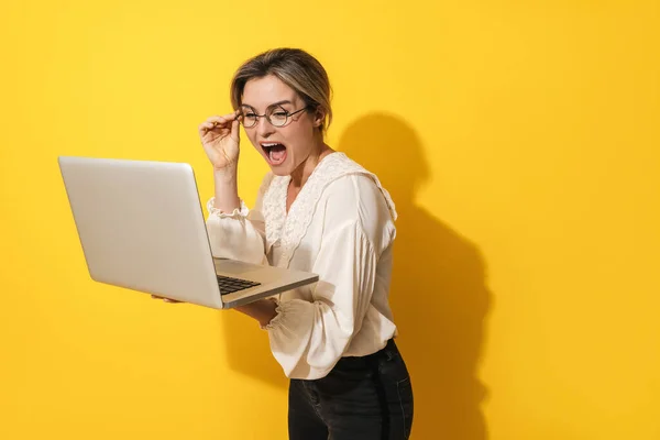 戴着眼镜的快乐的年轻女子正在用黄色背景的笔记本电脑 — 图库照片