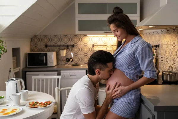 Young and sensual couple waiting for a baby. Husband and his pregnant wife during breakfast time in cozy kitchen.