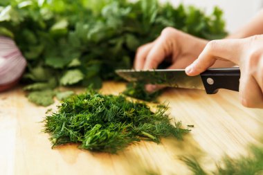 Bıçaklı kadın eli, tahta kesme tahtasının dereotunu kesiyor.