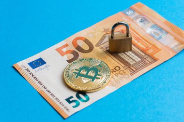 Parlak altın bir bitcoin ve 50 avroluk banknota küçük bir pirinç kilit yakın çekim.