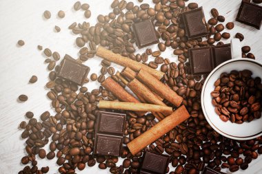 Bir yığın kızarmış kahve çekirdeği, tarçın çubukları ve koyu çikolata.