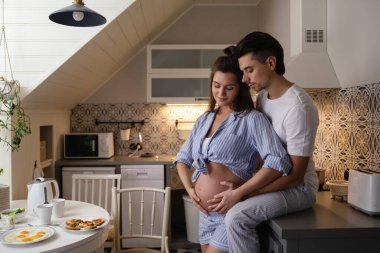 Bebek bekleyen genç ve şehvetli bir çift. Koca ve hamile karısı kahvaltı saatinde rahat mutfakta..