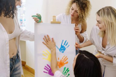 Avuçlarıyla çizen bir grup genç kadın renkli gökkuşağı renkleri kullanarak LGBT topluluğunu desteklemek için modern sanat eserleri yaratıyorlar.