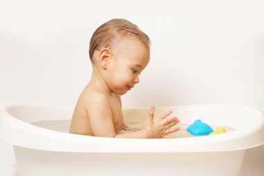 Sevimli gülümseyen küçük çocuk sıcak suda yüzen plastik oyuncaklarla banyo yapıyor..