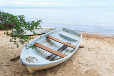 Sakin deniz suyunun yakınındaki kumlu bir sahilde terk edilmiş eski püskü bir balıkçı teknesinin yakın çekimi..