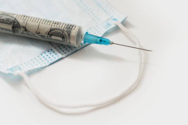 Tek kullanımlık hijyenik bir maskenin üzerinde duran yuvarlak bir dolar banknotla dolu plastik şırınga. covid-19 sonuçları ve hastalık önleme harcamaları kavramı.