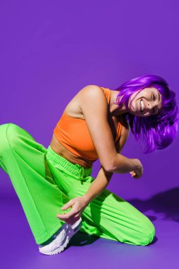 Dertsiz aktif kadın dansçı renkli spor giyerek mor arka plana karşı gösteri yapıyor.