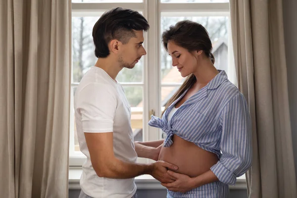若い官能的なカップルが赤ちゃんを待っています 男と彼の妊娠中の妻は窓のそばで抱き合って — ストック写真