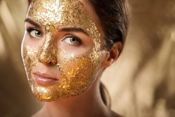 Beautiful young woman with golden shining mask on her face for skin treatment