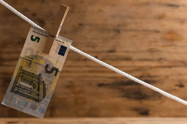 Five euro banknote is drying on a white rope, held by laundry pin. Councept of money saving or money laundering.