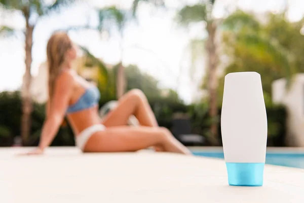 stock image White plastic bottle of skin care product with a young woman in bikini resting near the pool on background.