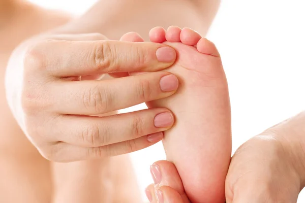Closeup shot of a mother gently massaging her little child\'s feet and soles on white background.