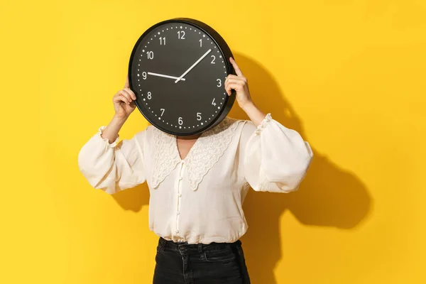 時間管理の概念 女性カバー彼女の顔で大きな時計上の黄色の背景 — ストック写真