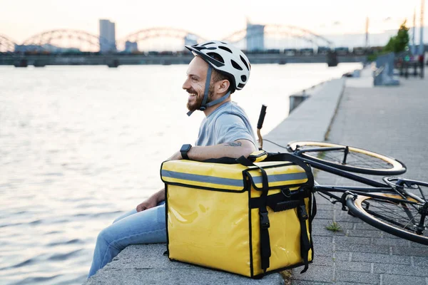 Young Smiling Express Delivery Courier Sitting Quay Looking Quiet River — Stock Photo, Image