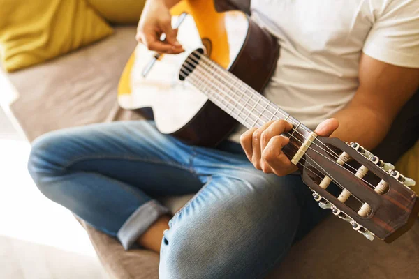 Joven Sentado Sofá Está Tocando Casualmente Guitarra Acústica Una Habitación —  Fotos de Stock