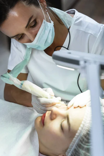 Professional permanent makeup artist and her client during lash line enhancement treatment