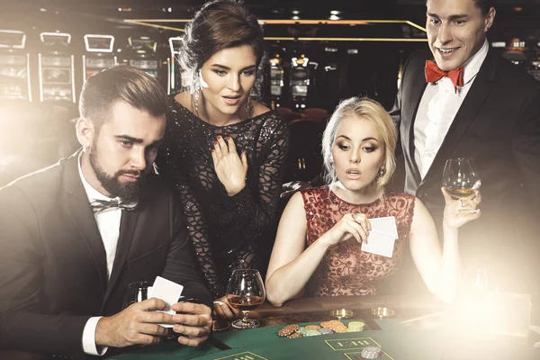 Group of young rich people playing poker and drinking cognac in the casino