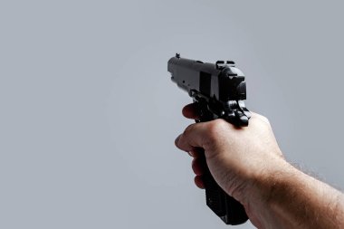Gri arka planda siyah tabancalı ilk erkek eli görüntüsü.