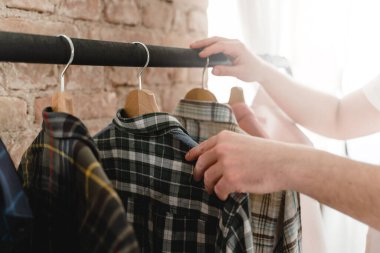 Adam gardıroptaki elbise rafında asılı çeşitli gömleklerini karıştırıyor.