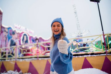 Sıcak kıyafetler giymiş neşeli ve şık bir kadın, karlı bir kış eğlence parkında eğleniyor..