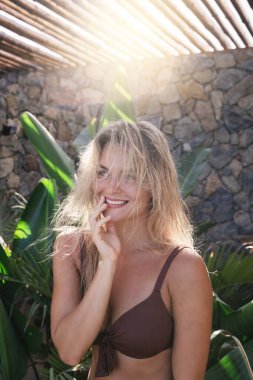Açık havada kahverengi bikini giyen, tropikal muz yapraklı genç bir kadın.