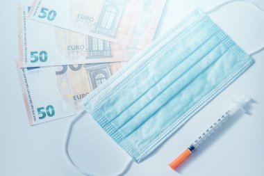 Tek kullanımlık yüz maskesi, şırınga ve 50 Euro 'luk banknotlar. Covid-19 'dan sonra ortaya çıkan mali kriz kavramı.