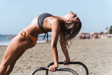 Sahildeki spor salonunda spor yaparken paralel barlarda esneme hareketleri yapan genç bir bayan sporcu..