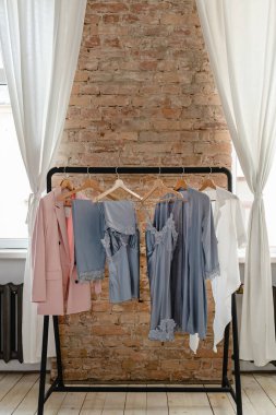 Elbise askısı, çeşitli şık kadın kıyafetleriyle odada dimdik duruyor. Hepsi de ahşap askılarda sallanıyor.