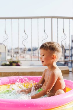 Küçük çocuk sıcak bir yaz günü balkonda şişirilebilir yuvarlak bir yüzme havuzunda neşeyle oynar..