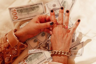 Altın yüzüklerle süslenmiş zengin bir adamın elleri ve Amerikan dolarlarının arka planında çarpıcı siyah bir manikür..