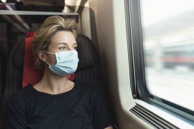 Yolculuğu sırasında trene binen tıbbi maske takan genç bir kadının portresi.