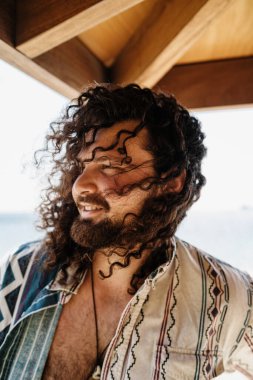 Yaz güneşli bir günde sahilde dinlenen kaygısız kıvırcık adamın portresi.