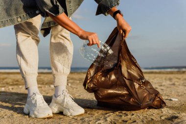 Kadın gönüllü, doğayı temiz tutma çabalarına katkıda bulunmak için plajda plastik atık topluyor. Plastik şişeyle yakın plan..
