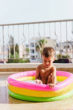 Küçük çocuk sıcak bir yaz günü balkonda şişirilebilir yuvarlak bir yüzme havuzunda neşeyle oynar..