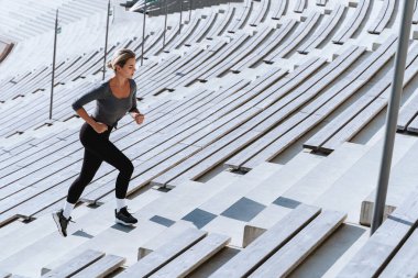 Spor giyinen kadın sporcu açık hava stadyumunun tribünleri arasında merdivenlerde koşuyor ve egzersiz yapıyor..