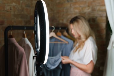 Genç bir kadın ve farklı kıyafetleri olan bir elbise askısı. Küçük sergi salonunda moda tasarımcısı.